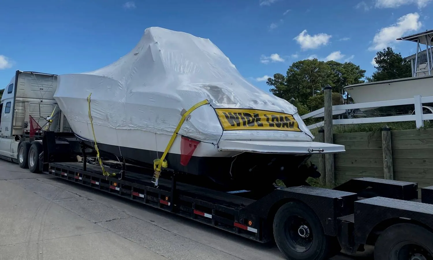 A shrink-wrapped hull on a drop deck with a wide load banner